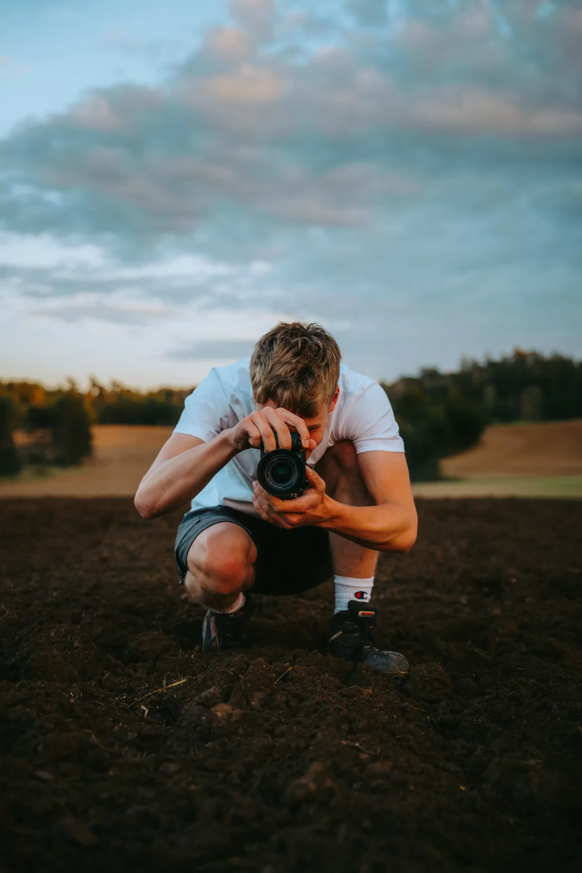 Fotograf kniet mit Kamera auf einem frisch bearbeiteten Acker im Abendlicht